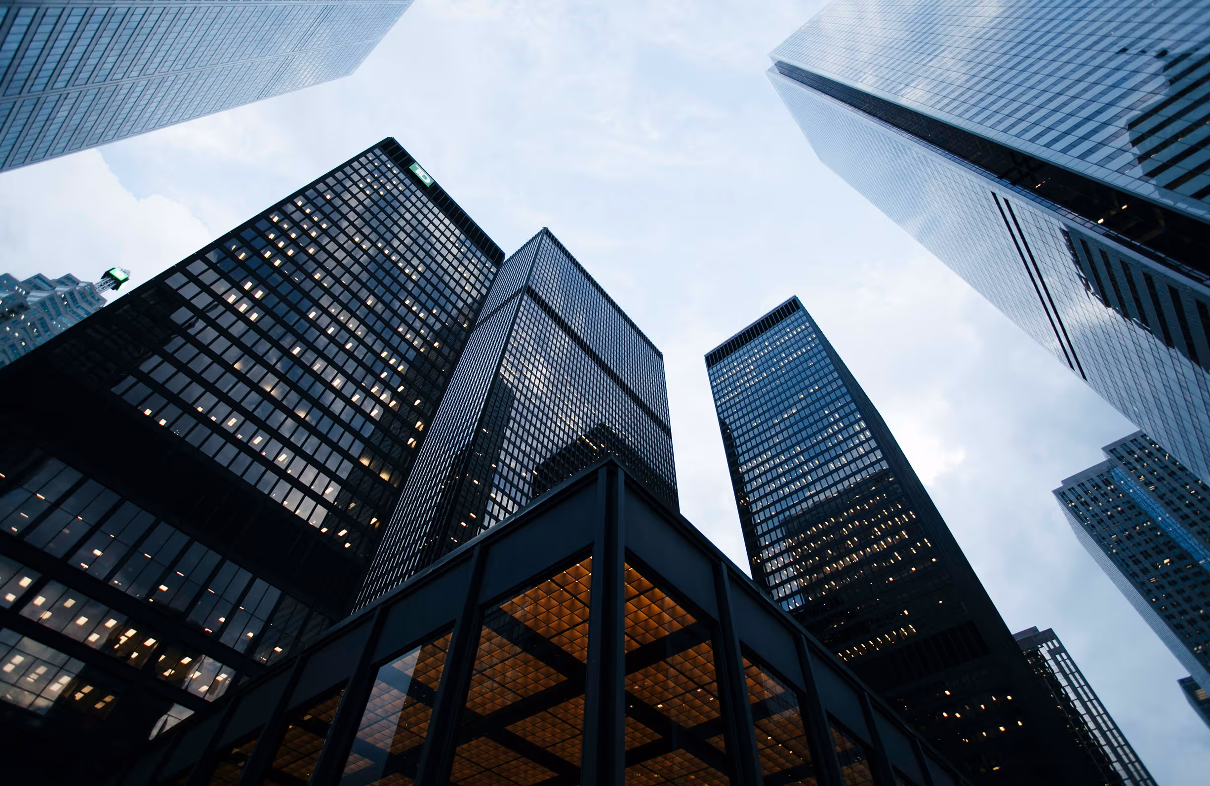 Low-angle view of tall modern skyscrapers with glass facades against a cloudy sky at dusk.